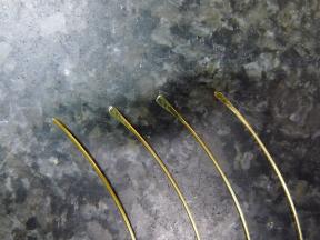 Der Herstellungsfortschritt der Auslöserfedern: unbearbeiteter Draht - plattgeschlagener Draht - gefeilte Spitze - fertig angespitzt